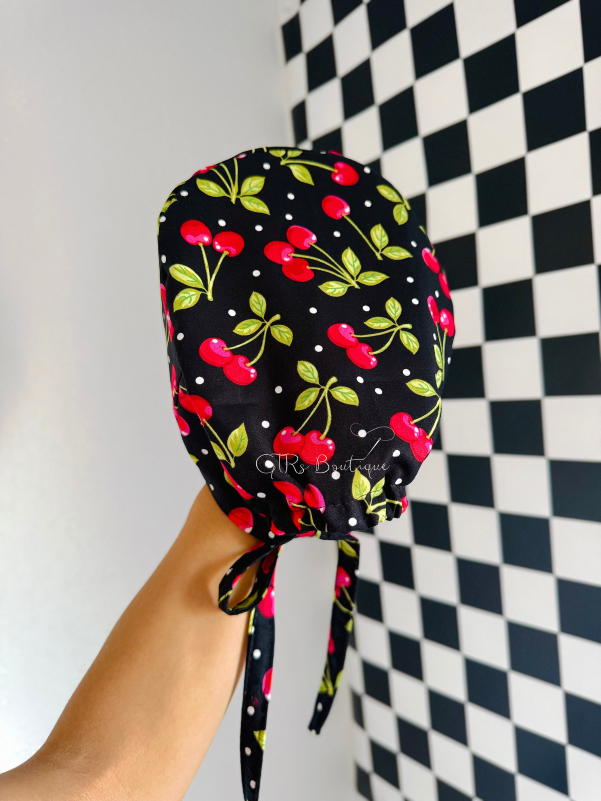 A black scrub cap with a red cherry print