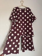 A two-piece matching lounge set consisting of a short-sleeve top and wide-leg pants in a dark burgundy ribbed fabric with large white polka dots, hanging on a gold hanger against a light gray wall.
