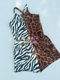 A sleeveless halter romper laid flat on a light blue textured background, featuring a split design with a black and white zebra print on the left and a brown leopard print on the right.